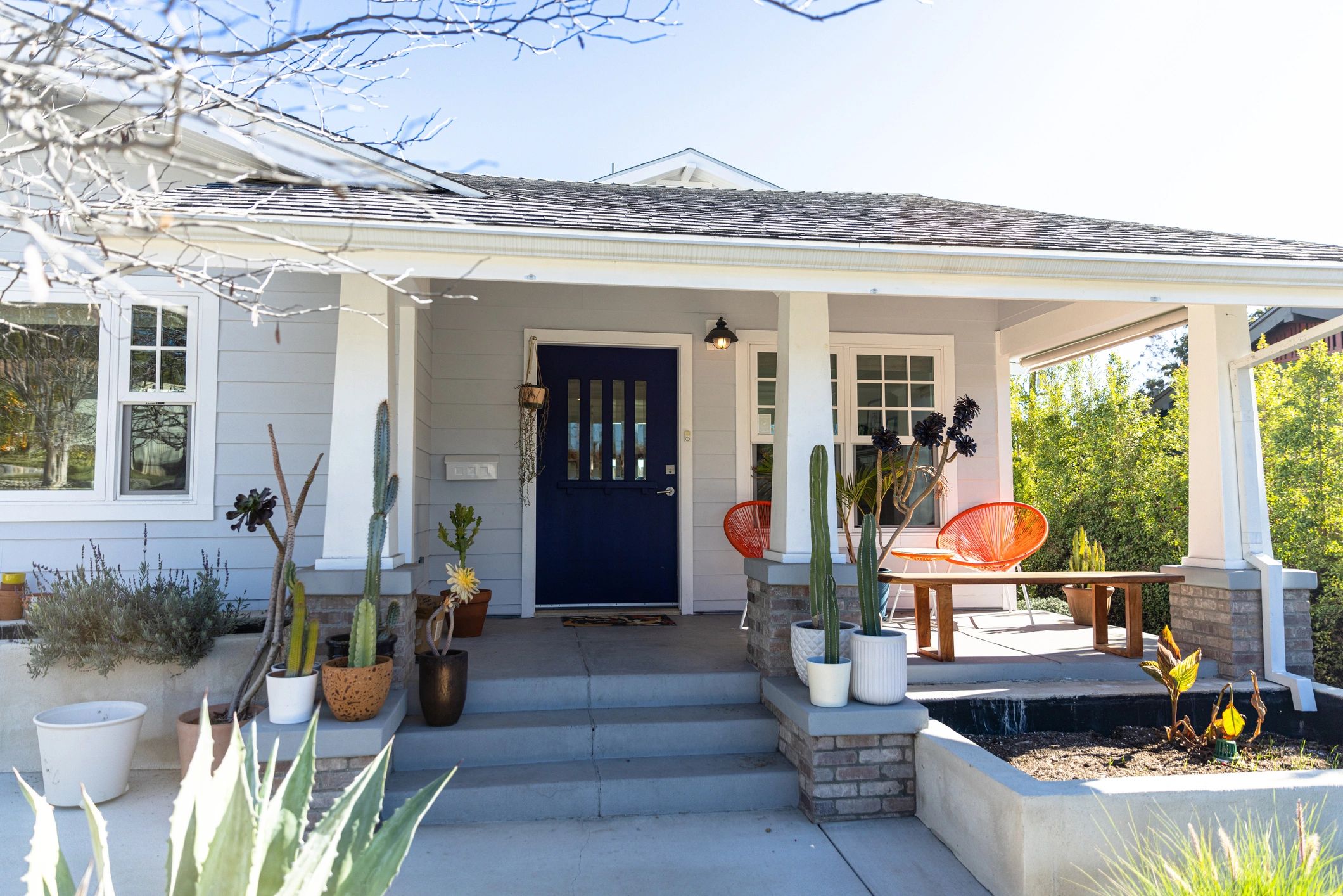 Bright front porch with blue door and potted plants.