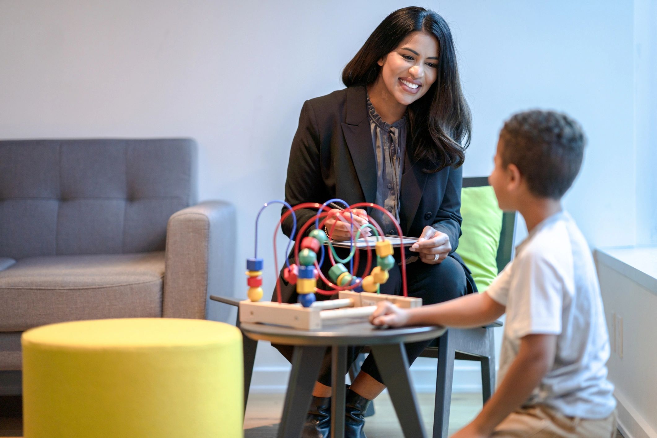 A woman engages a child with a bead maze toy in a cozy room.